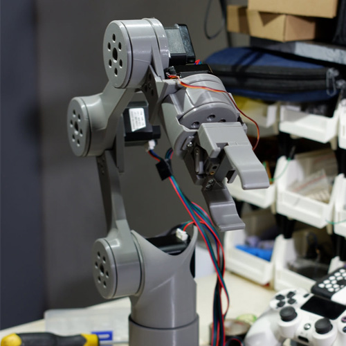 3D-printed robot arm stood upright on a bench with its control wiring running to the joints