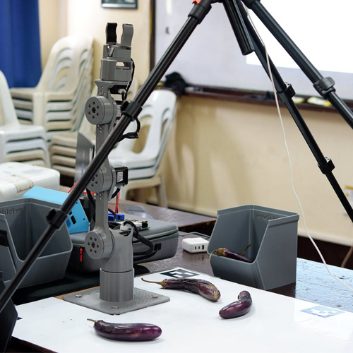 Printed robot arm reaching over a table in a classroom-style demonstration